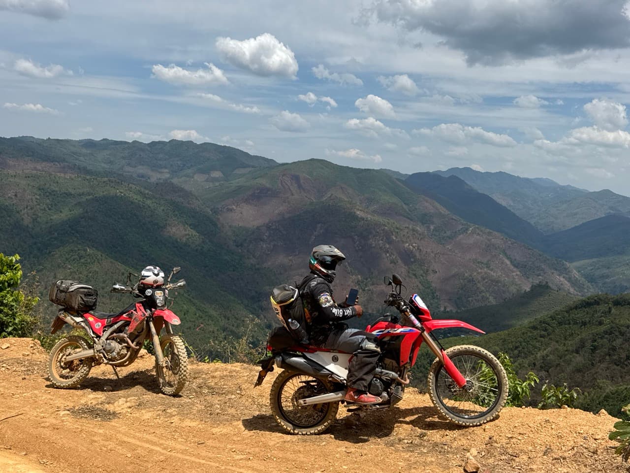 Riders stopped at a cliff-edge viewpoint over layered mountain ridges