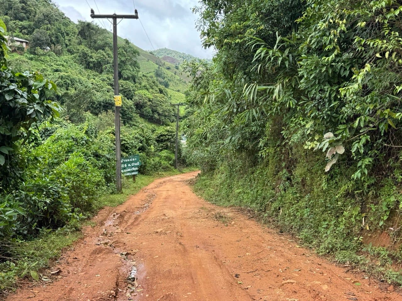 Red road into a village, with the village sign on the left.