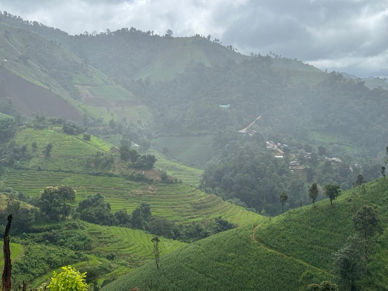 Terraced paddies and a village below, seen through rain haze.