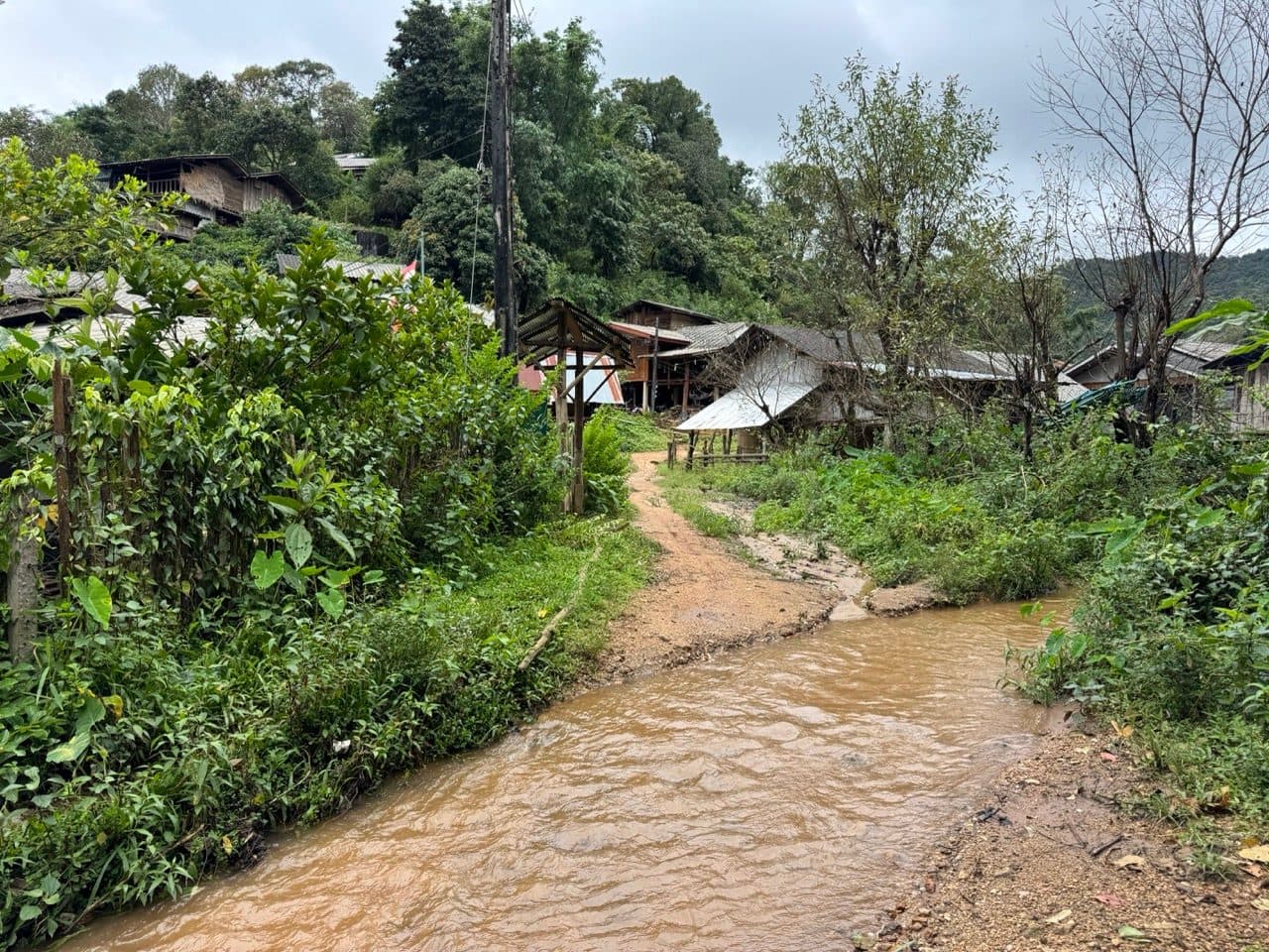 Karen village houses on a hillside above a stream running brown and full after rain.