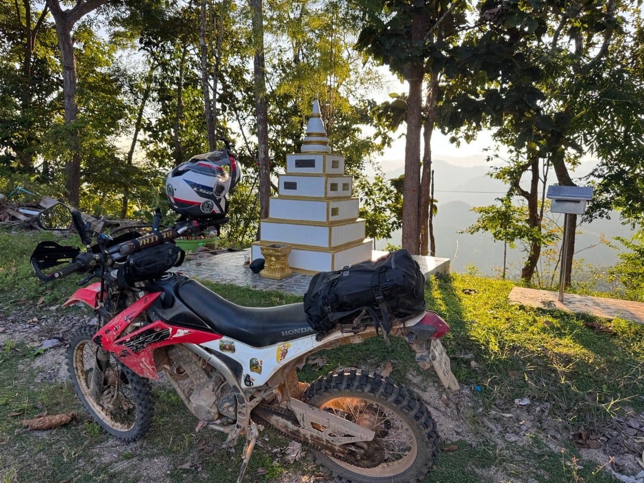 The 250 parked at the memorial chedi, late light on the hills.